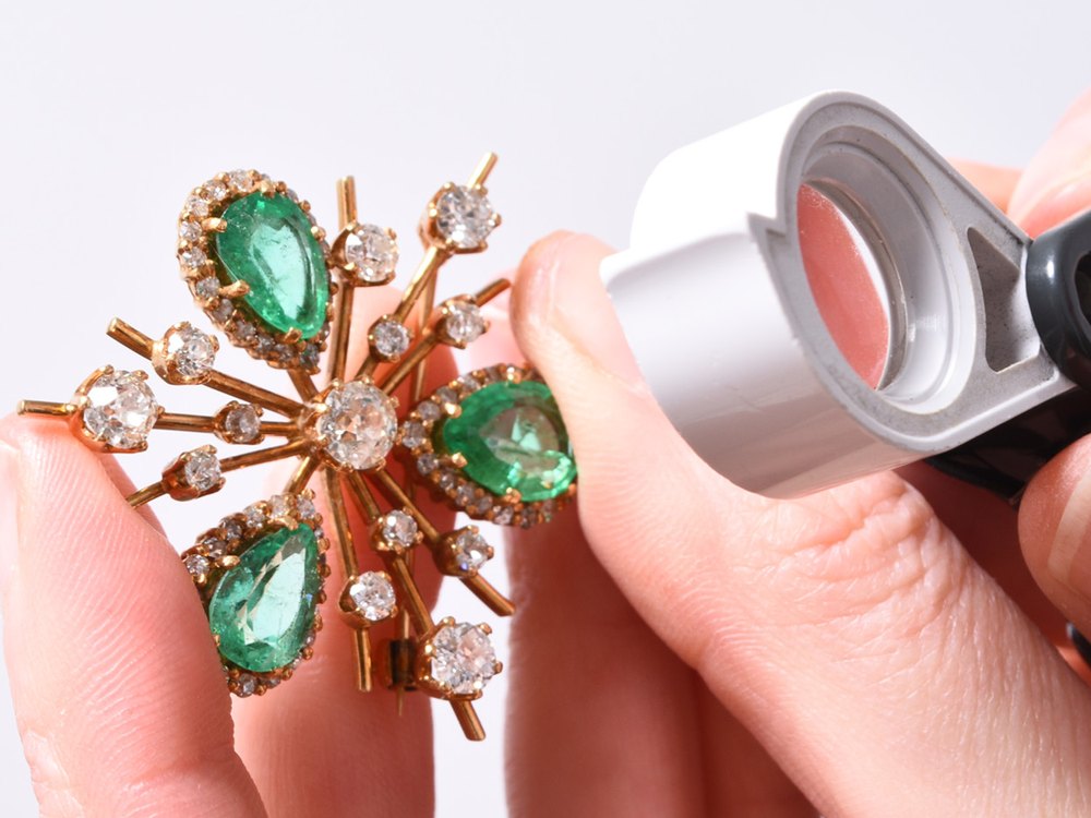 A Halls specialist examining a gem-set brooch with a loupe